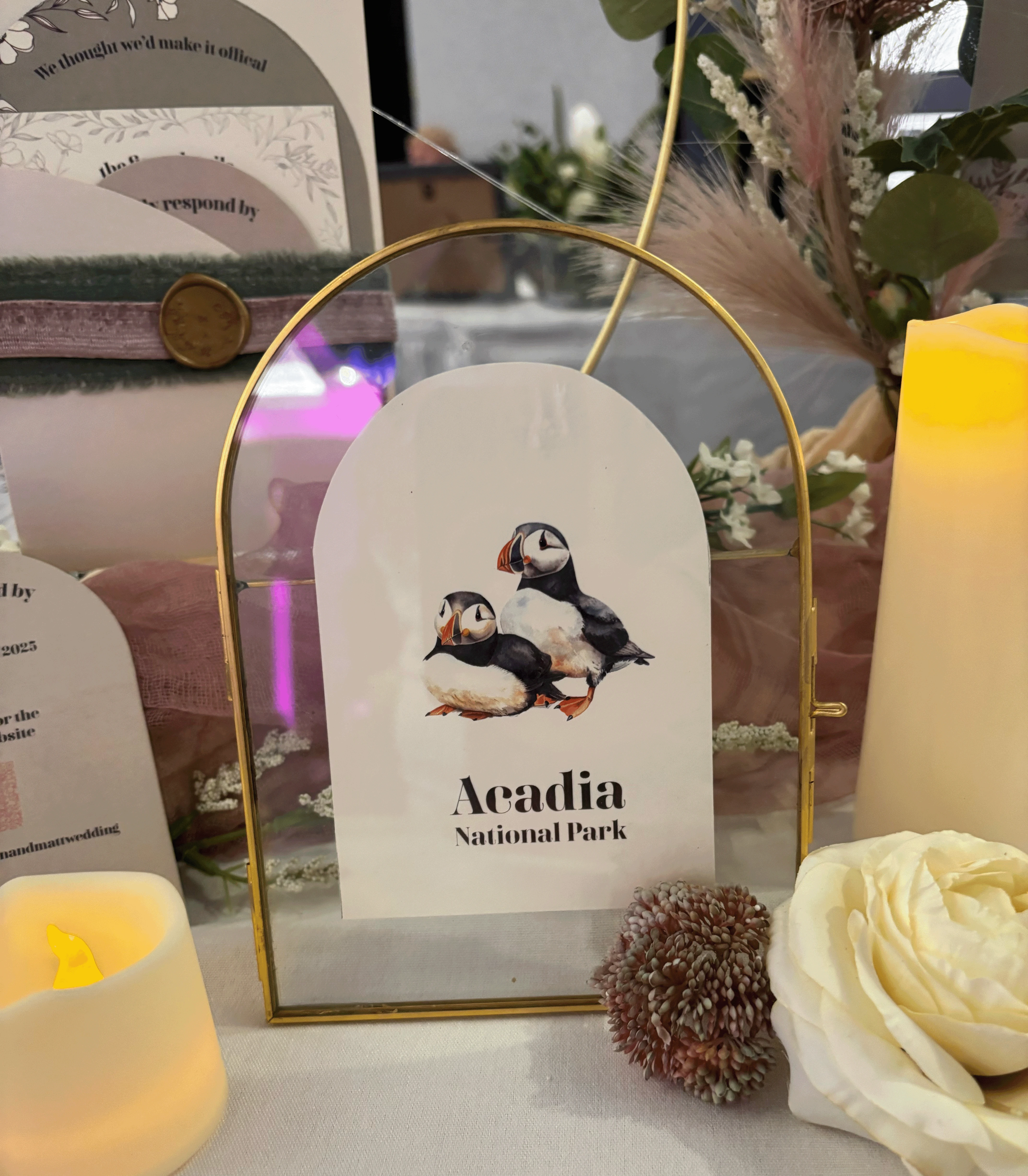 Table name sign in gold arc frame.  This sign is for Acadia National Park with two puffins.